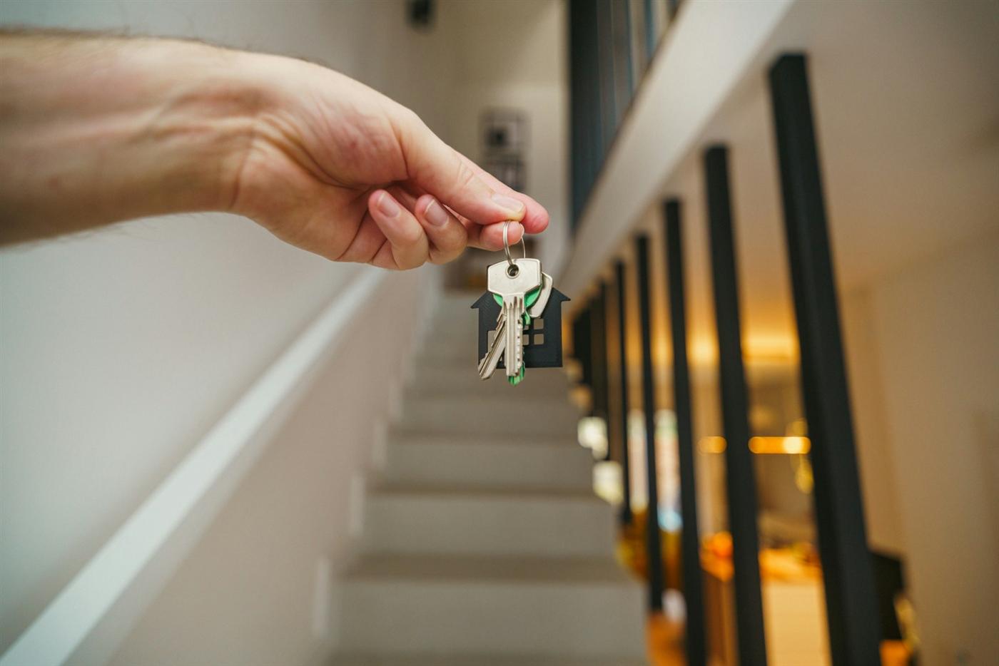 Una mano sostiene unas llaves frente a la escalera de una casa.