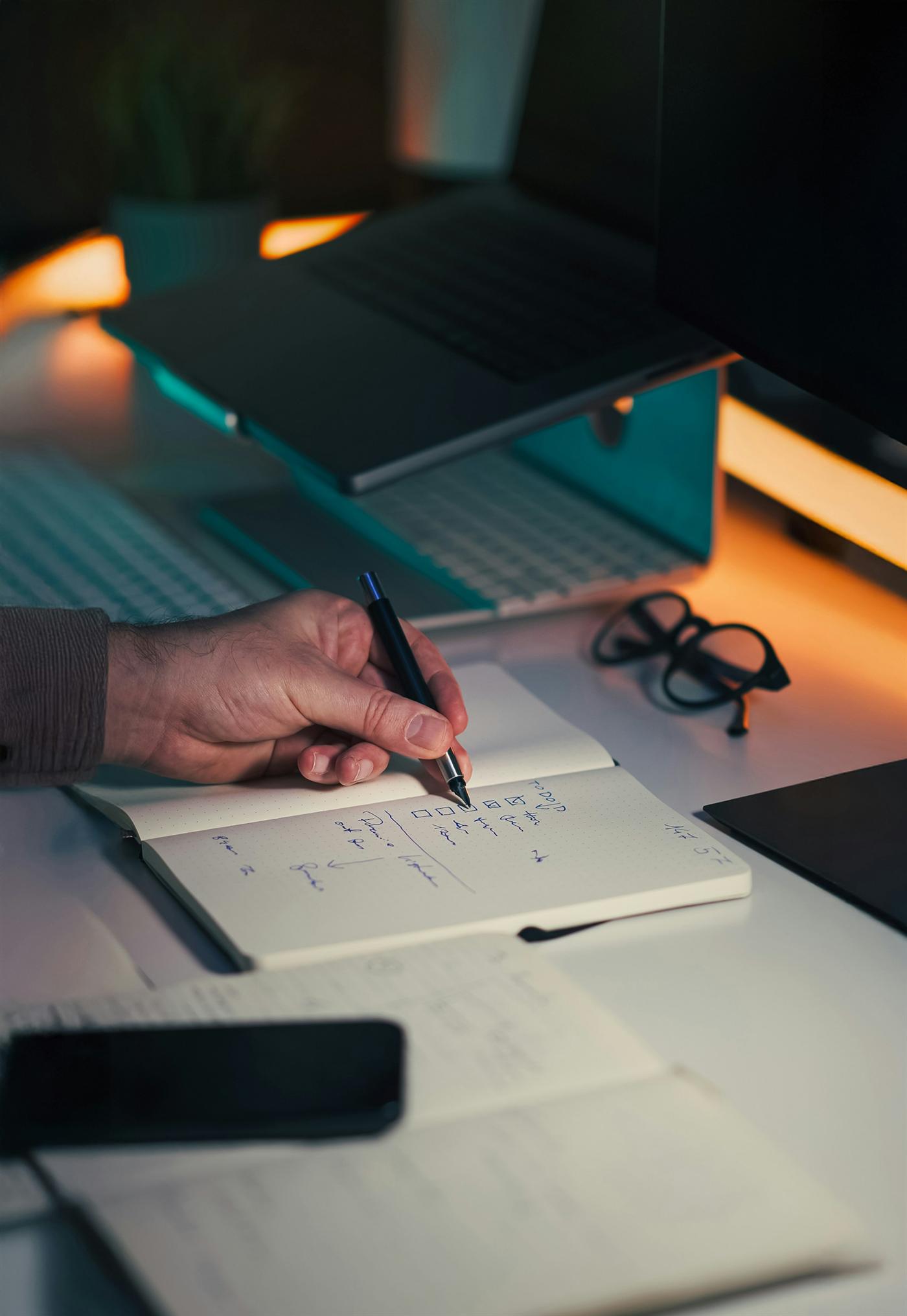 Una mano toma notas en un cuaderno junto a una computadora.